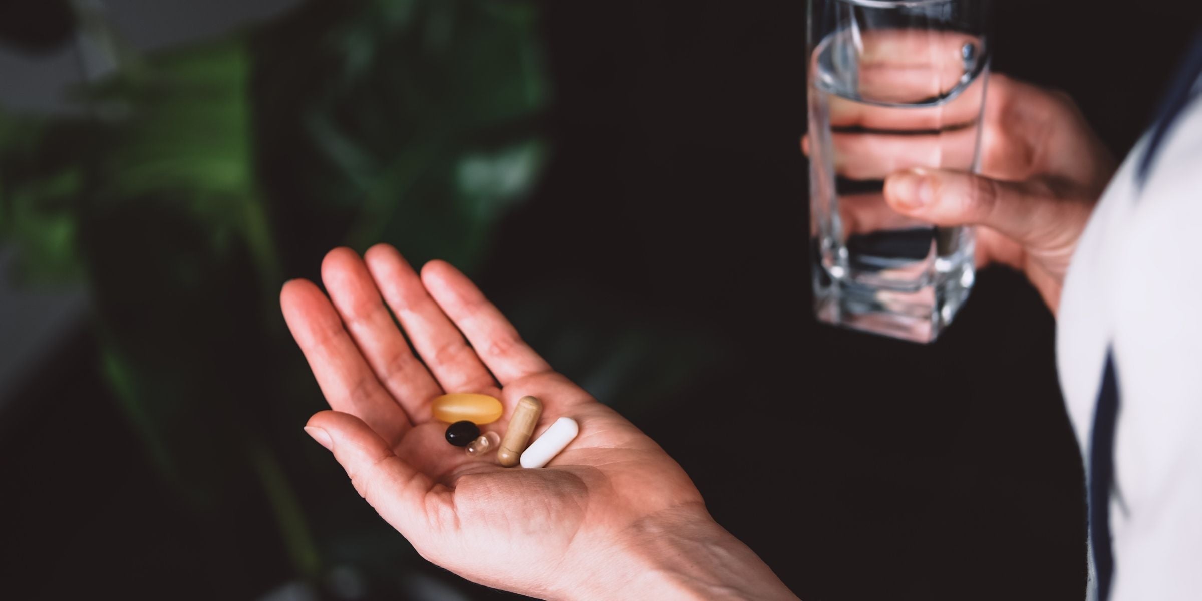 a person holding out their hand with supplements scattered with a glass of water