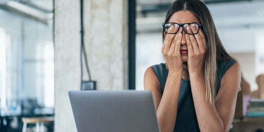 a woman looking stressed and rubbing her eyes at work