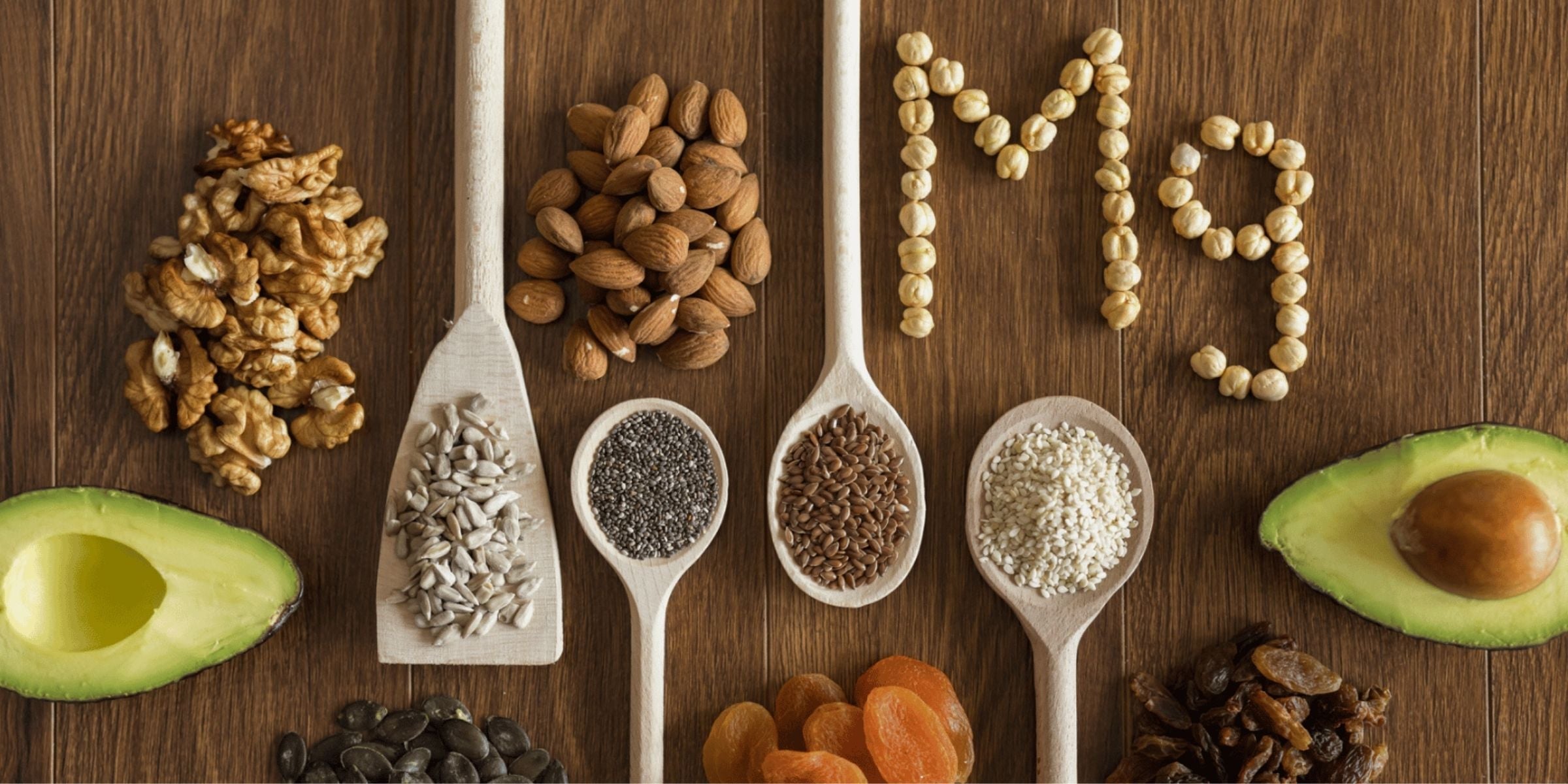 an artistic arrangement of various seeds and nuts, including an avocado half, placed on wooden spoons and around them