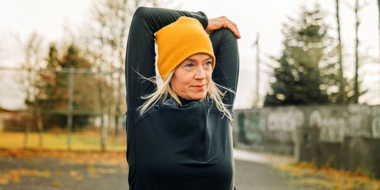 a woman wearing a beanie stretching outside in the cold