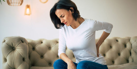 a woman sitting on a lounge while holding her back in pain