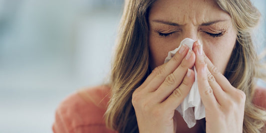 a woman suffering from hayfever and sneezing into a tissue